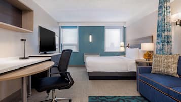 A hotel room with a desk, chair, bed, and sofa.