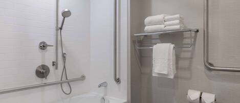 A modern bathroom with a walk-in shower, grab bars, a glass shelf with towels, and a toilet paper holder.
