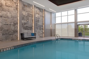Una piscina interior moderna con una pared de piedra, un área de descanso con sofá y ventanas amplias.