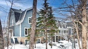 A large, two-story house with a steeply pitched roof, surrounded by snow-covered ground and trees. - Tremblant Prestige - Manoir 120-6 (Mont-Tremblant)