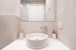 Een moderne badkamer met een ronde witte wastafel, een spiegel en een deur op de achtergrond.