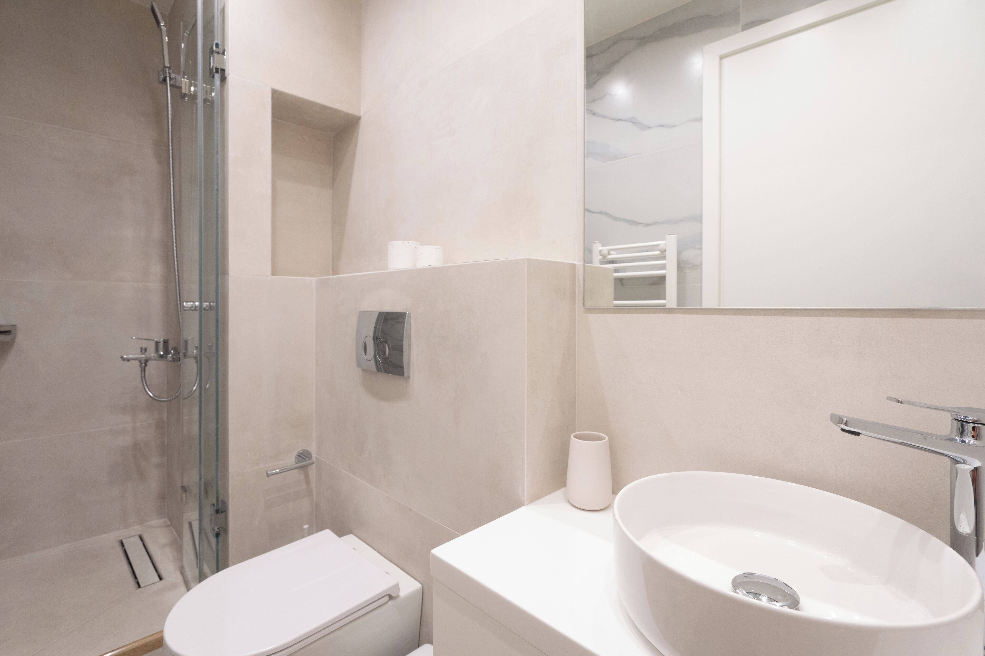 Een moderne badkamer met een douchecabine van glas, een wit toilet en een groot wastafelmeubel met een marmeren blad.