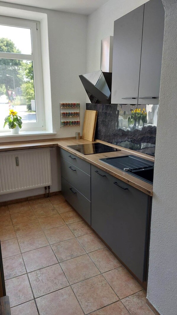 A modern kitchen with grey cabinets, a black countertop, and a window with a view of greenery.