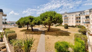 A courtyard with a paved walkway, neatly trimmed hedges, and a large tree. - Escape at Les Sables d'Olonne Harbour – Sleeps 4 (Les Sables-d´Olonne)