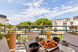 A balcony with a table set for breakfast, including croissants and a bottle of juice, overlooking a residential area with trees and buildings. - Escape at Les Sables d'Olonne Harbour – Sleeps 4 (Les Sables-d´Olonne)