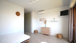 A minimalist bedroom with a bed, a wooden dresser, a television, and a small round table. - Studio for 4 with swimming pool and parking (Canet-en-Roussillon)