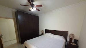 A bedroom with a bed, a ceiling fan, a nightstand, and a wardrobe.