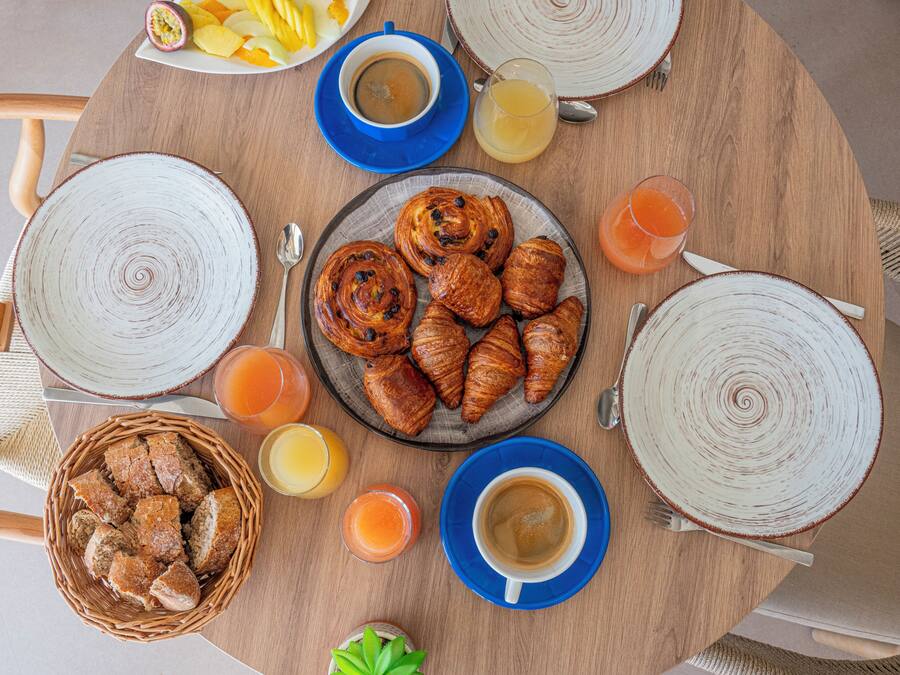 A round wooden table with breakfast items including croissants, bread, and orange juice.