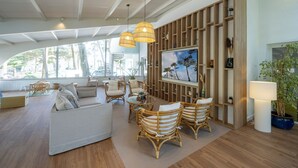 A spacious living area with a large window, a sofa, wicker chairs, a TV, and a wooden shelving unit. - Hôtel Punta Lara (La Gueriniere)