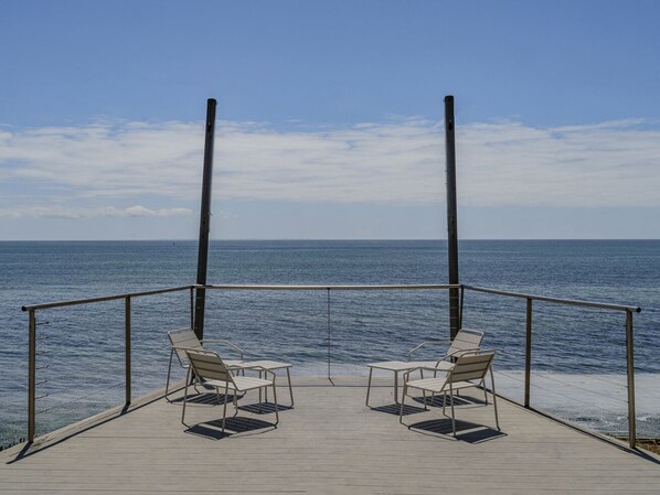 A wooden deck with two chairs facing the ocean.