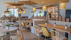 A modern restaurant interior with wooden tables and chairs, woven ceiling lamps, and a variety of plants. - Hôtel Punta Lara (La Gueriniere)