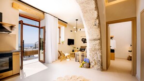 A modern kitchen with a built-in oven, a dining area with a table and chairs, and a living space with a sofa and a coffee table. - Mirthea Suites (Agios Vasileios)
