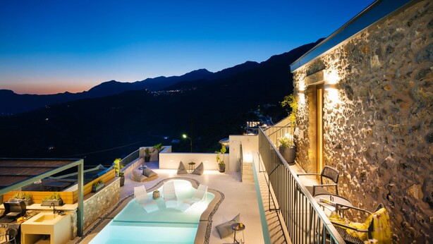 A rooftop pool area with a stone wall and a view of mountains. - Mirthea Suites (Agios Vasileios)