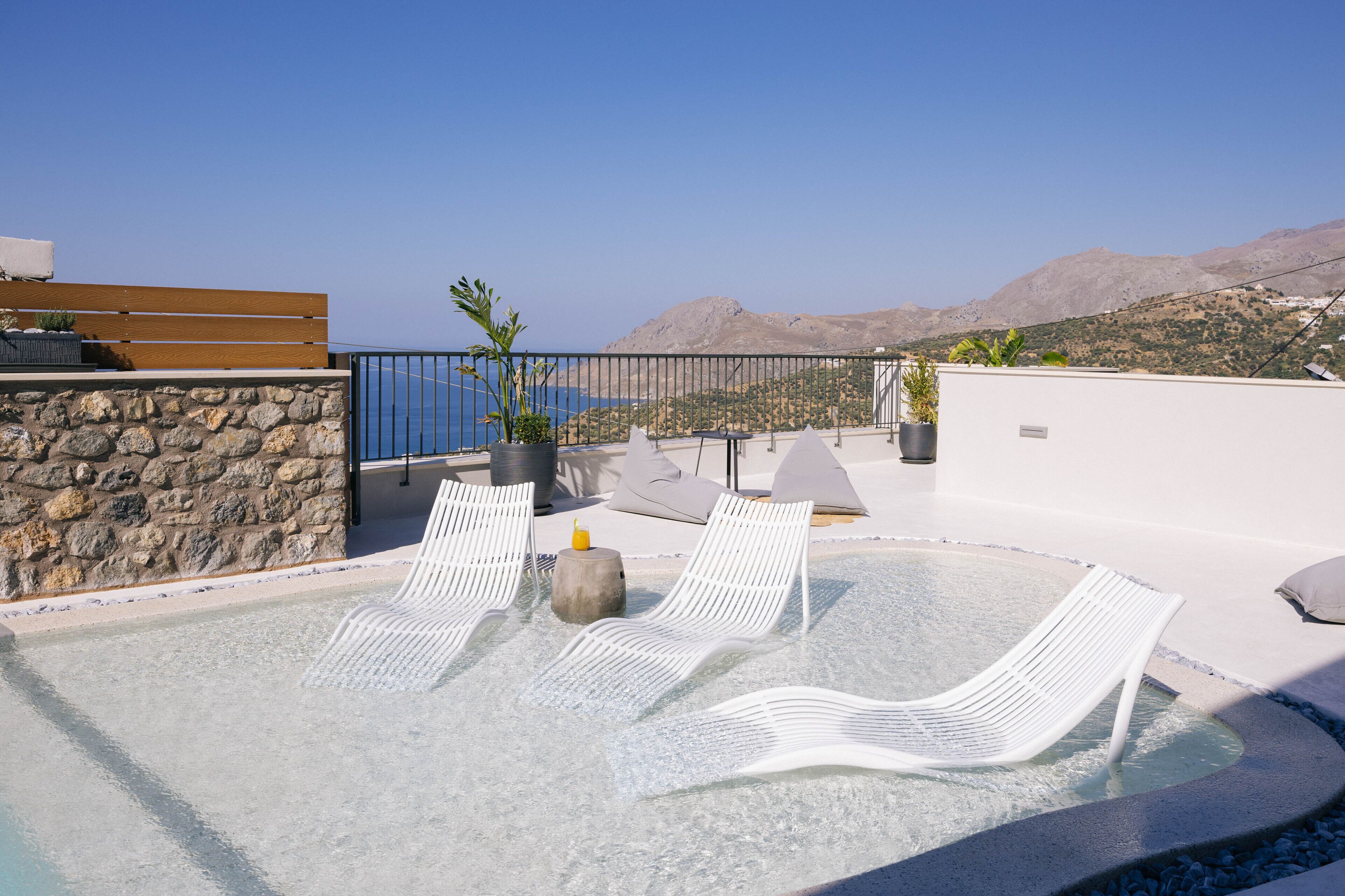 Un área de piscina en la azotea con sillones blancos y un muro de piedra.