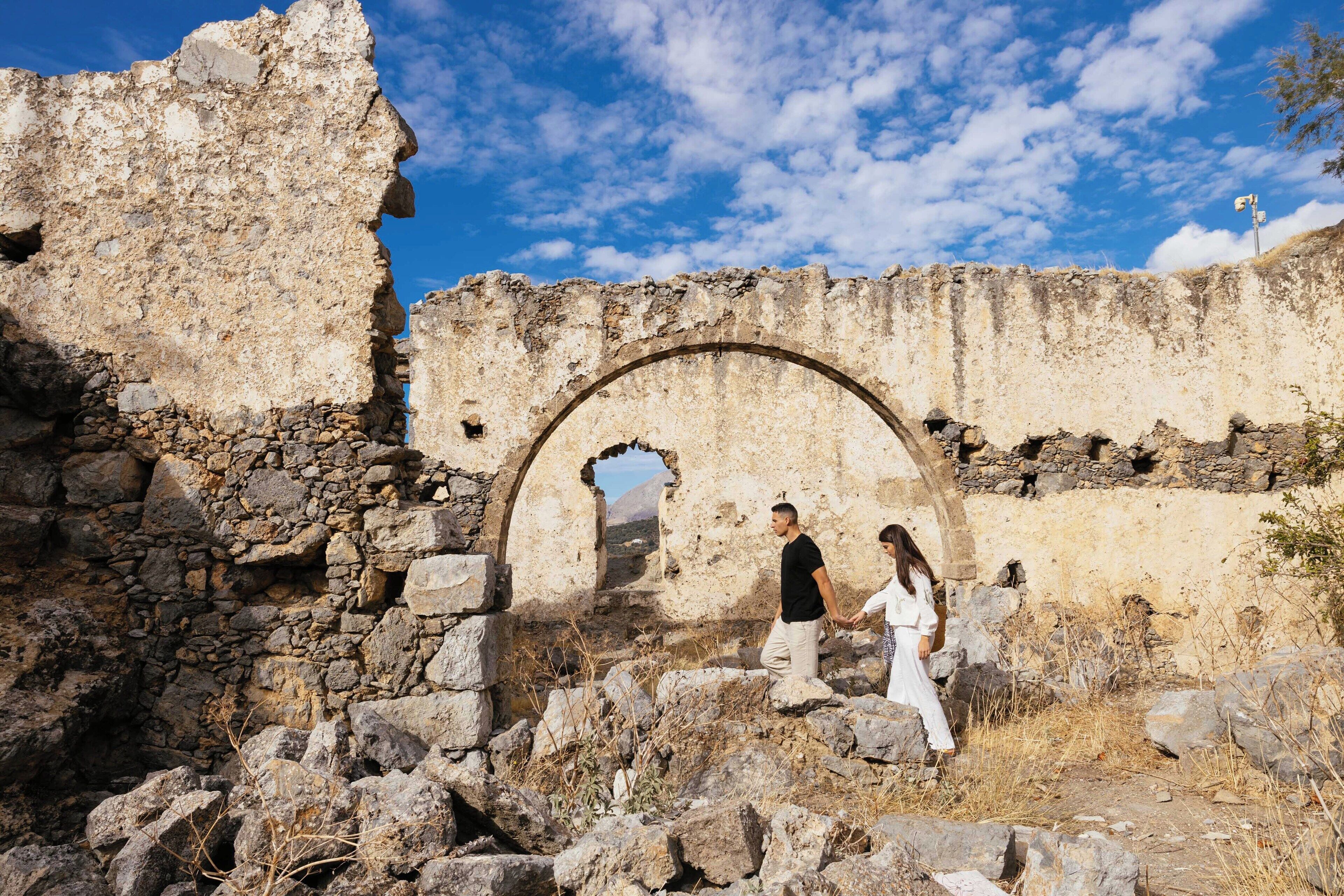 Une ancienne construction en pierre, dotée d’un grand portail en arc de cercle, entourée de ruines et de végétation desséchée.