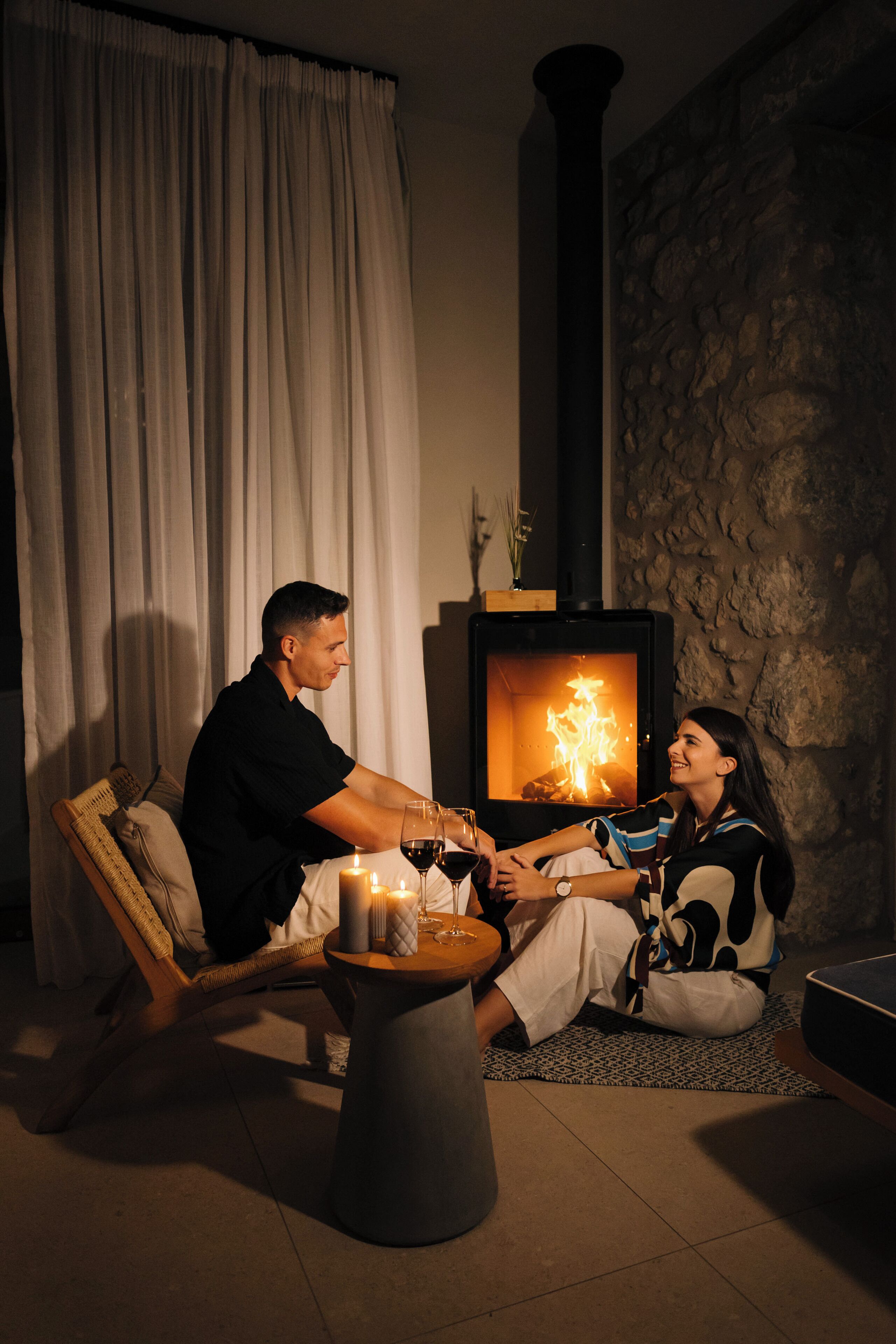 A cozy room with a fireplace, a sofa, a small table with candles, and a stone wall.