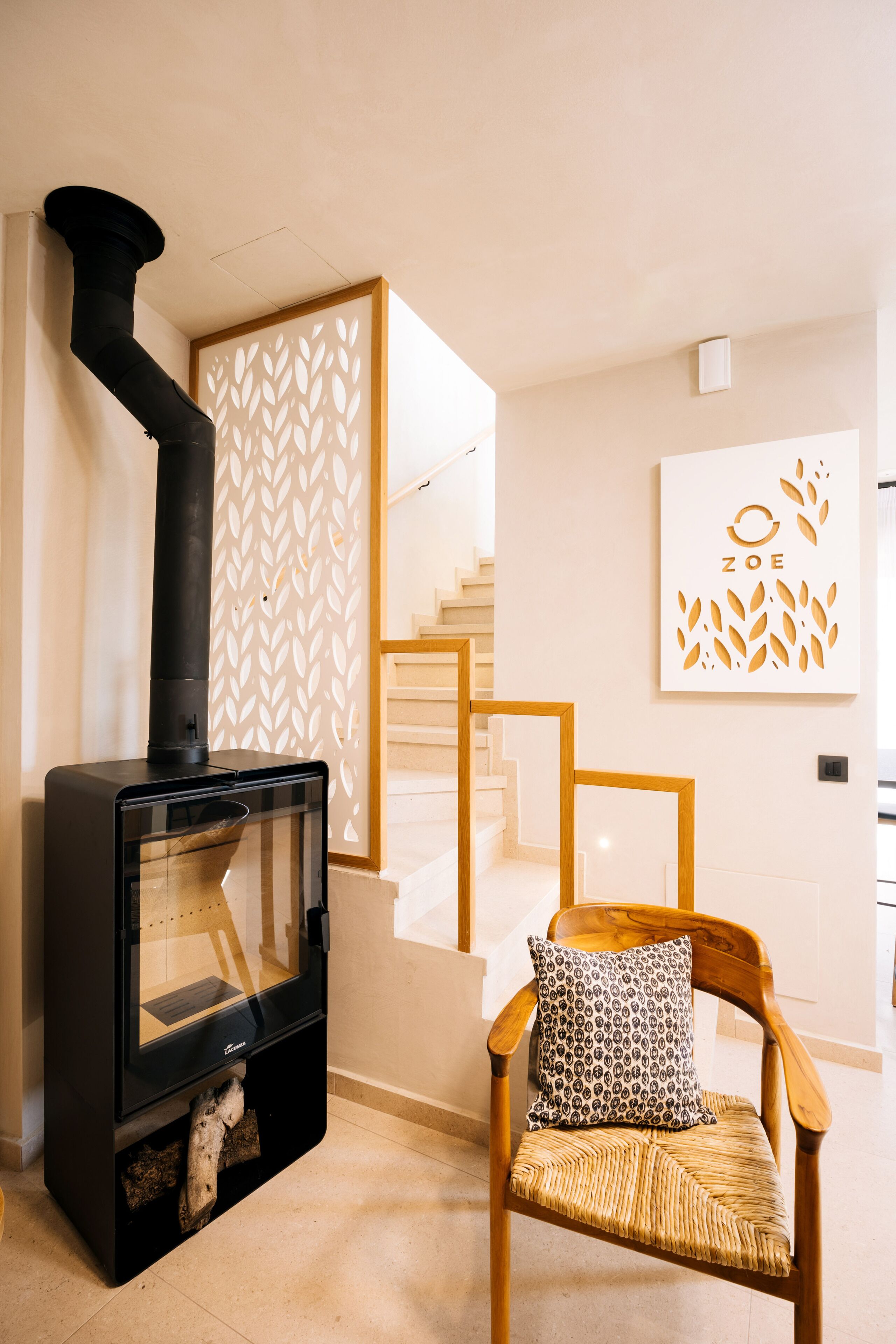 Una sala de estar moderna con una estufa de leña, una silla de madera con un cojín estampado y una escalera con un diseño geométrico en la pared.