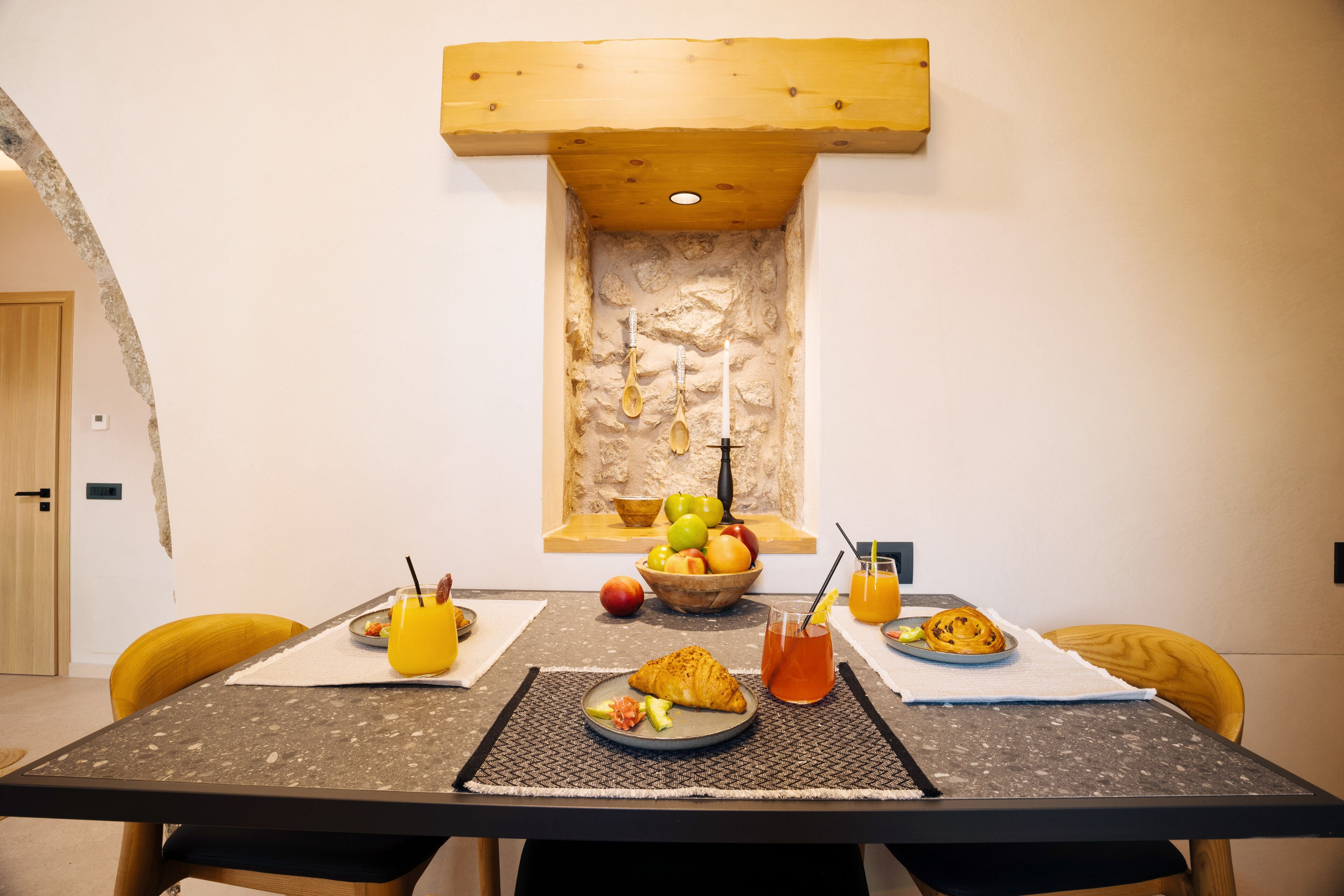 Une table à manger avec un croissant, un panier de fruits et des boissons.