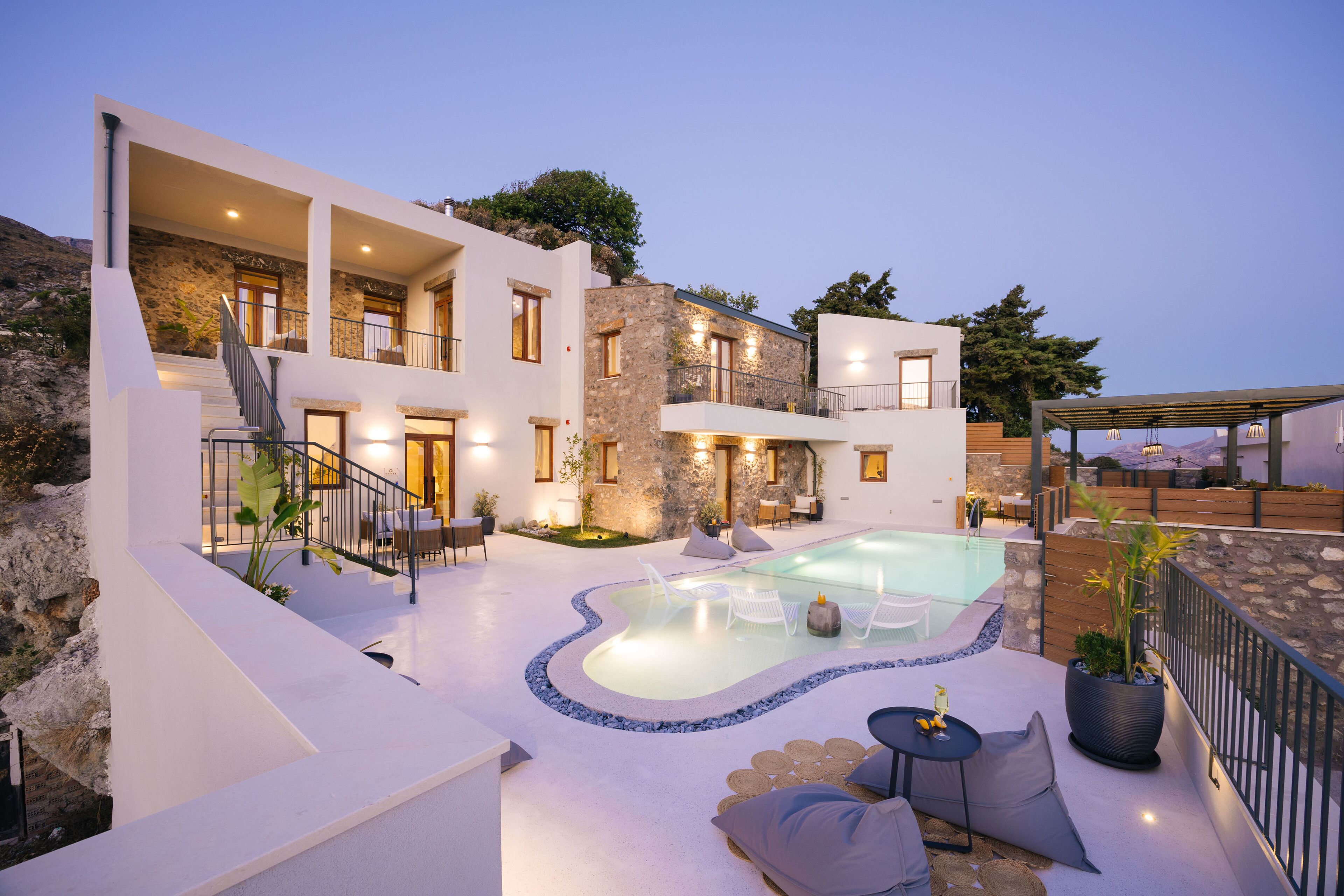 A modern villa with a swimming pool, outdoor seating, and a stone facade.