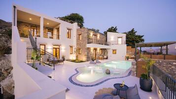A modern villa with a swimming pool, outdoor seating, and a stone facade.
