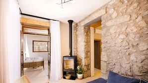 A cozy room with a stone wall, a sofa, a wicker chair, and a fireplace. - Mirthea Suites (Agios Vasileios)