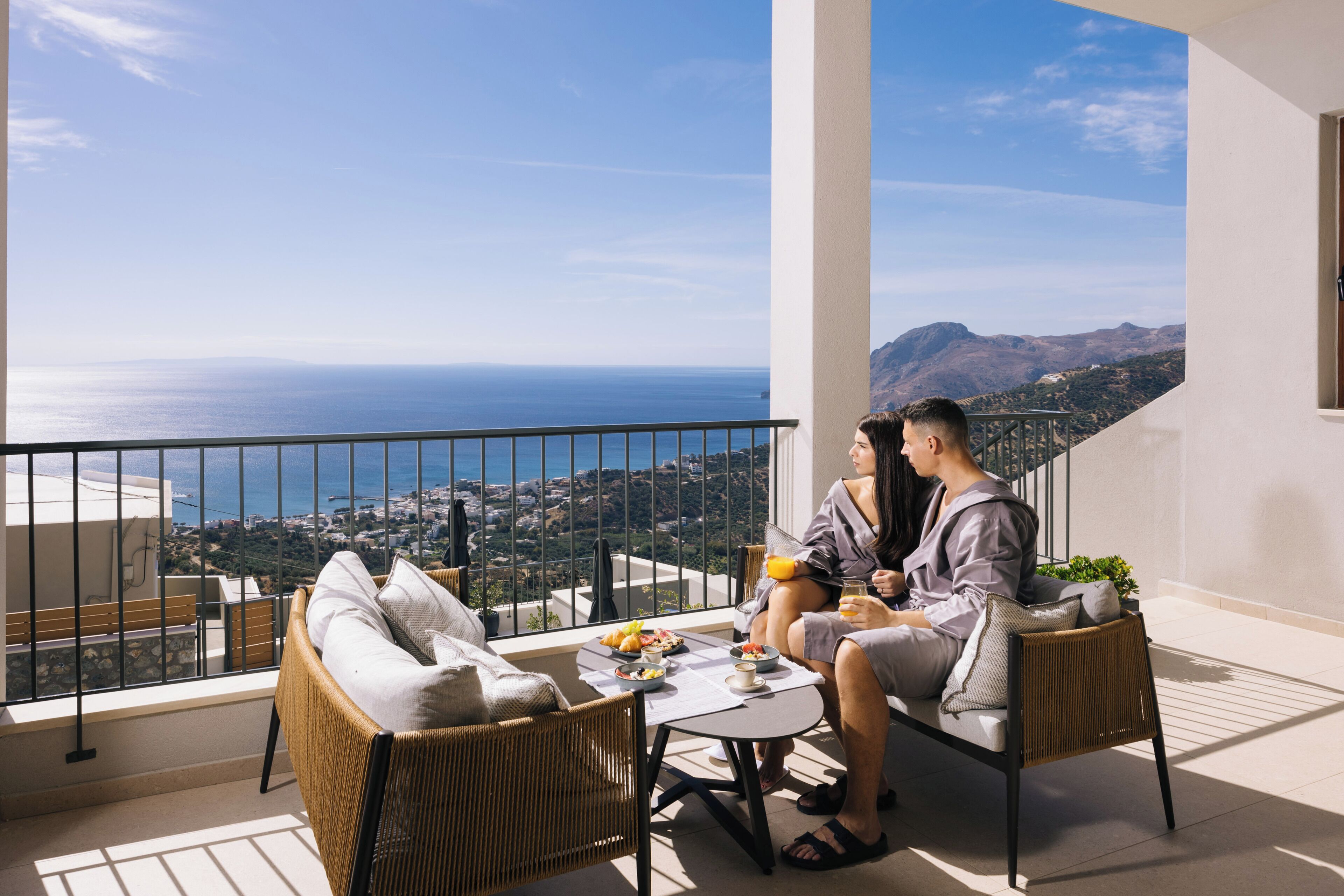 A balcony with wicker furniture, a table with breakfast items, and a scenic ocean view.