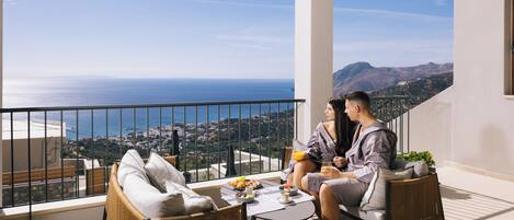 A balcony with wicker furniture, a table with breakfast items, and a scenic ocean view.