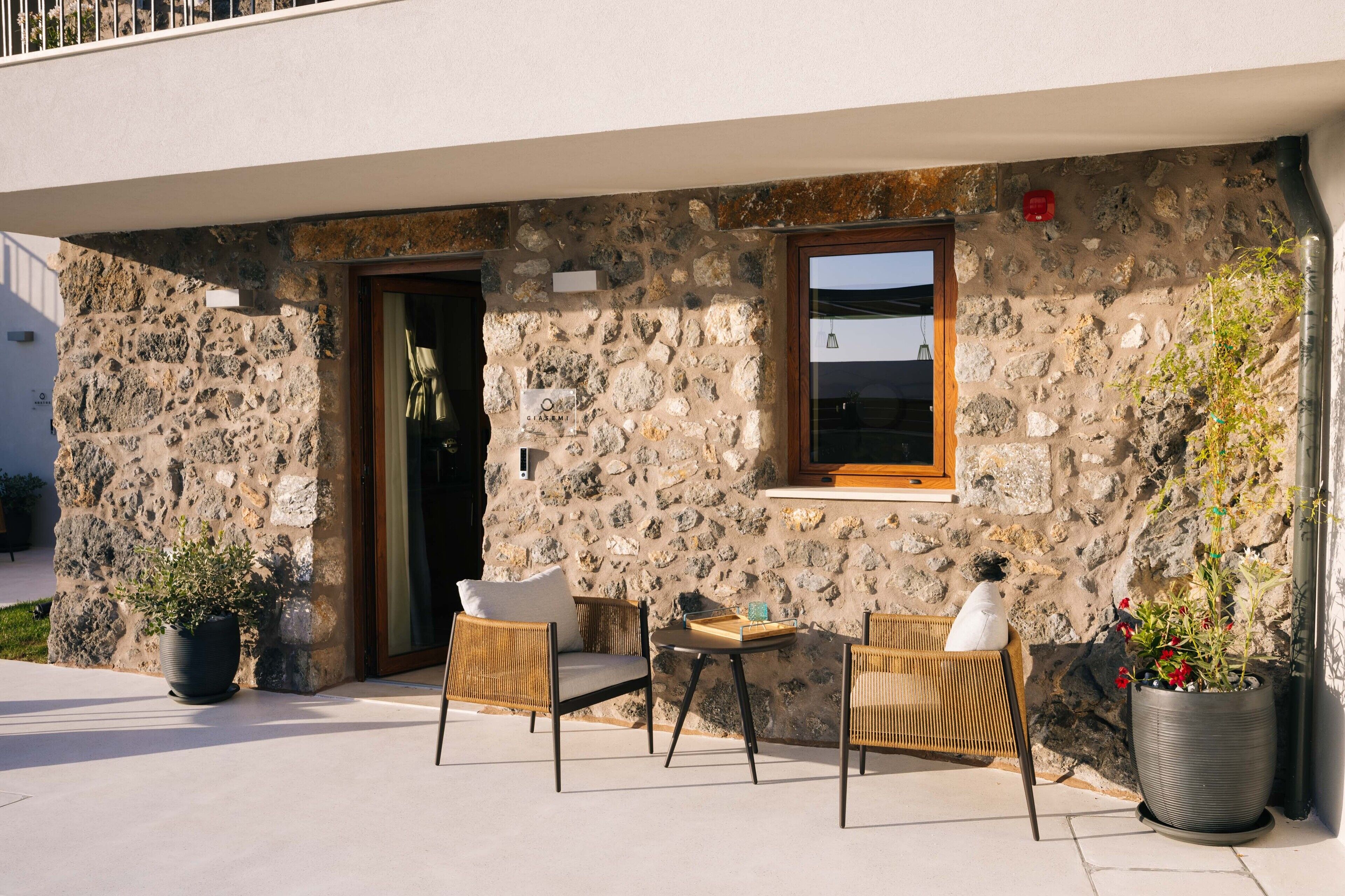 A stone building with a wooden door, two wicker chairs, a small table, and potted plants.