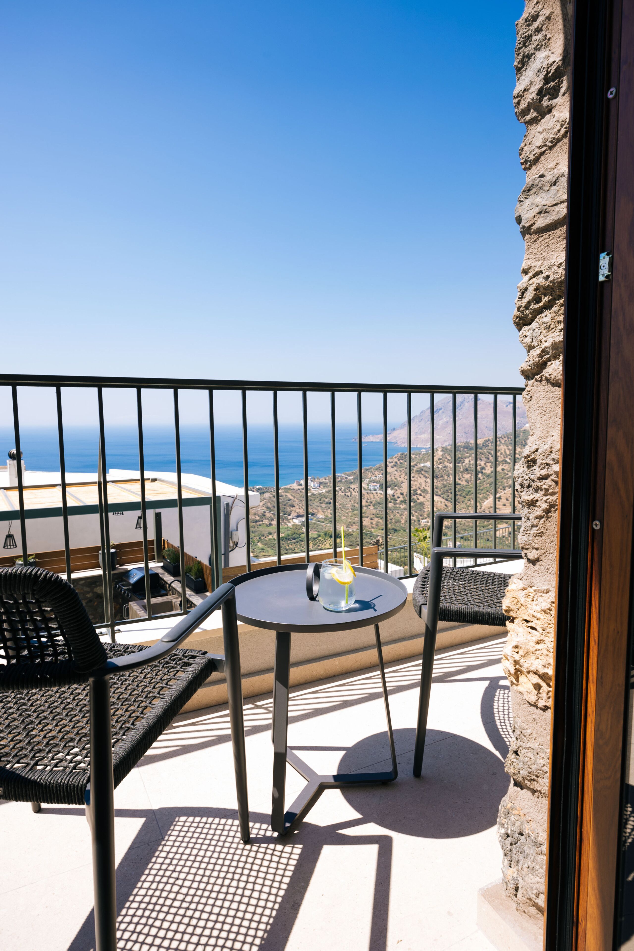 A balcony with a table and chairs, overlooking a coastal landscape.