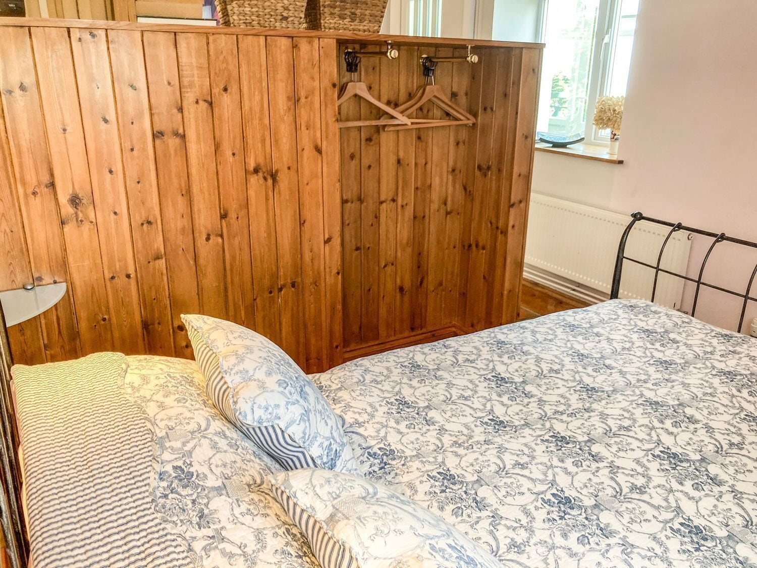 Een slaapkamer met een houten garderobe, een bed met een beddengoed met patroon, en een metalen bedframe.