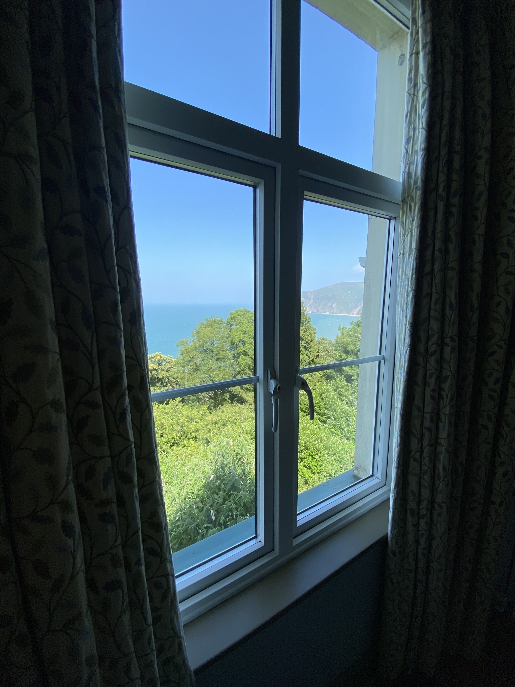 A window with a view of a coastal landscape, curtains, and a metal handle.