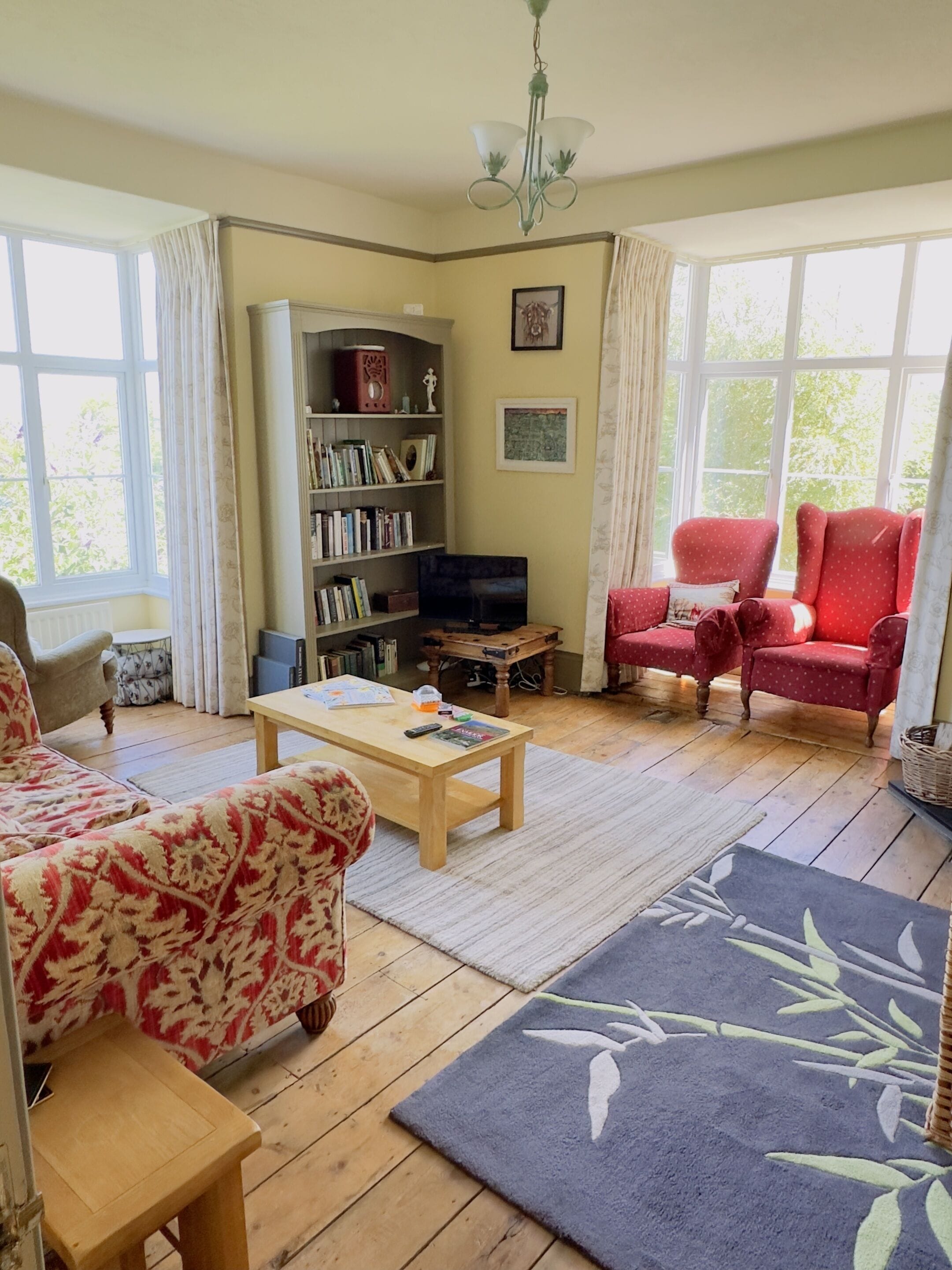A cozy living room with a bookshelf, a red armchair, a wooden coffee table, and a television.