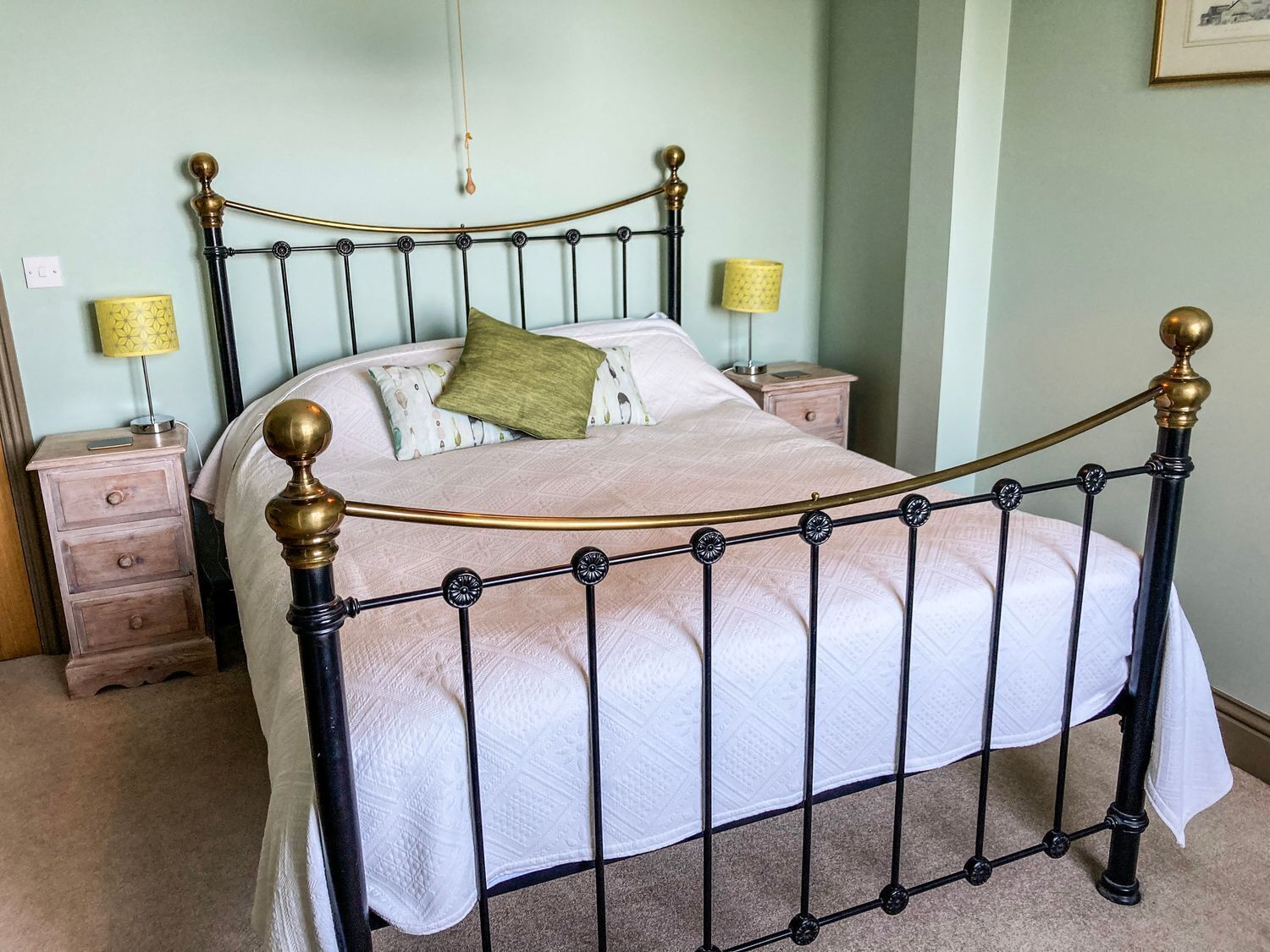 A bed with a metal frame and wooden headboard, two bedside tables with lamps, and a light green wall.