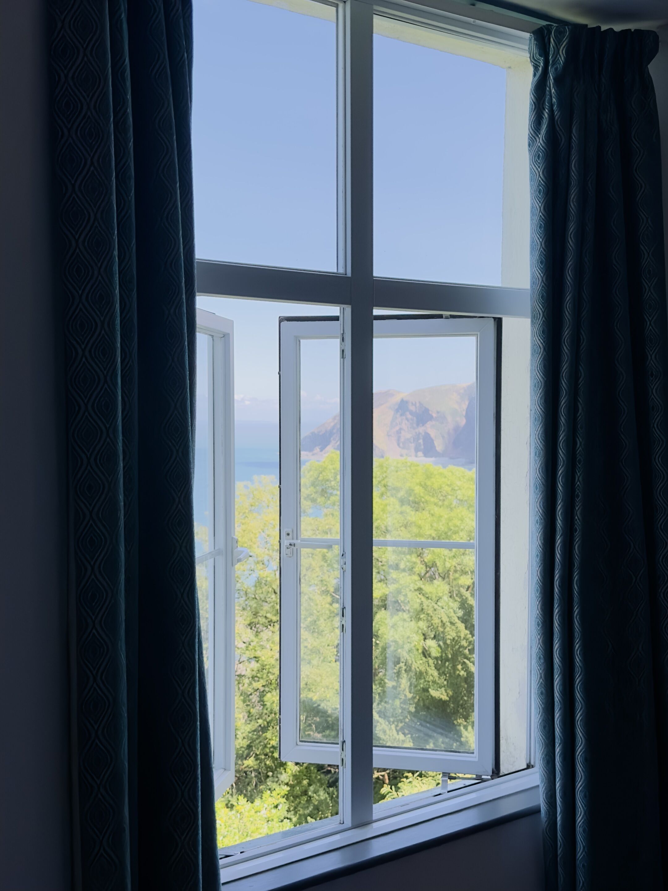 A window with a view of green trees and mountains.