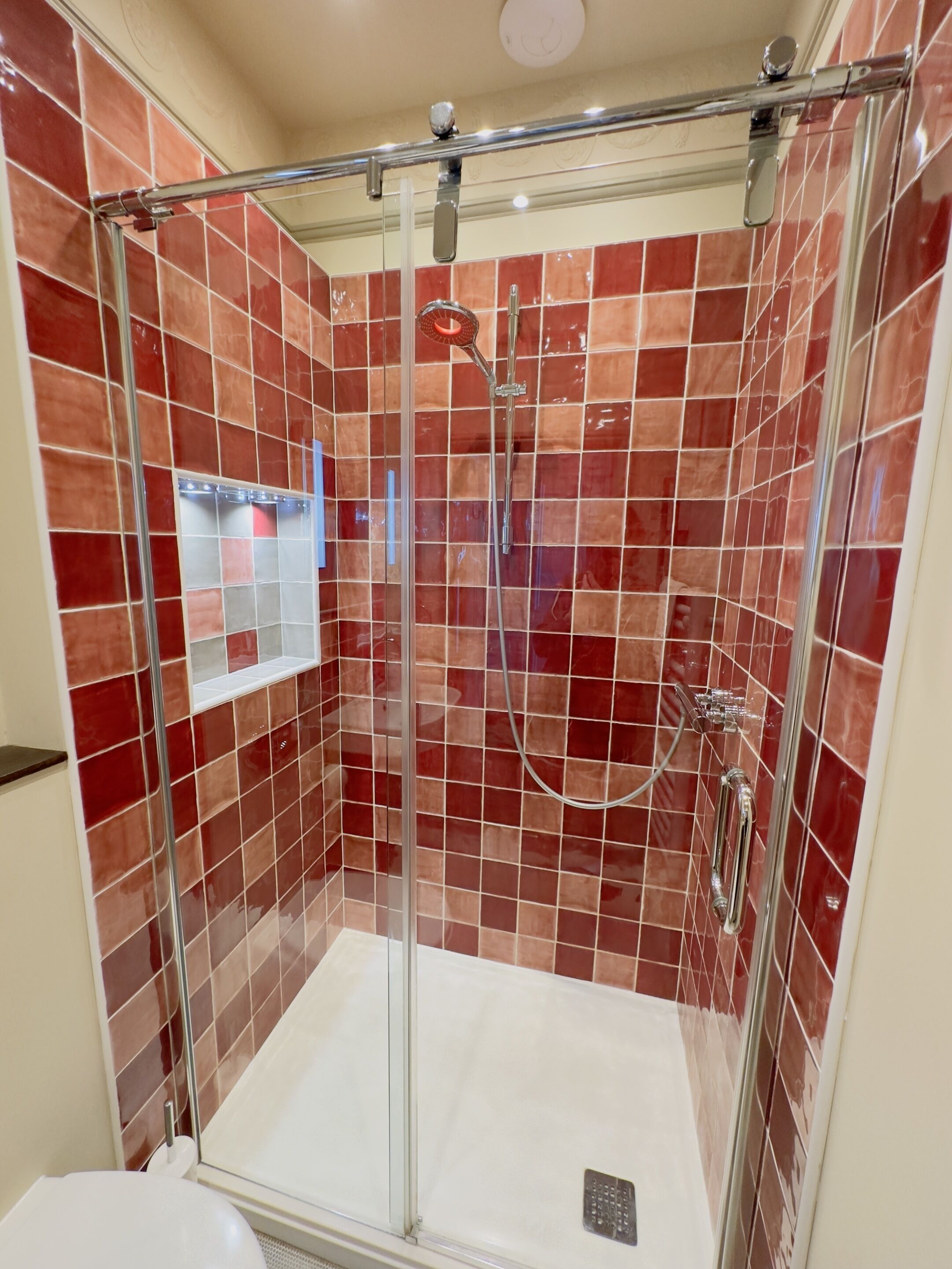 Un box de ducha con paredes de azulejos rojos y suelo blanco.