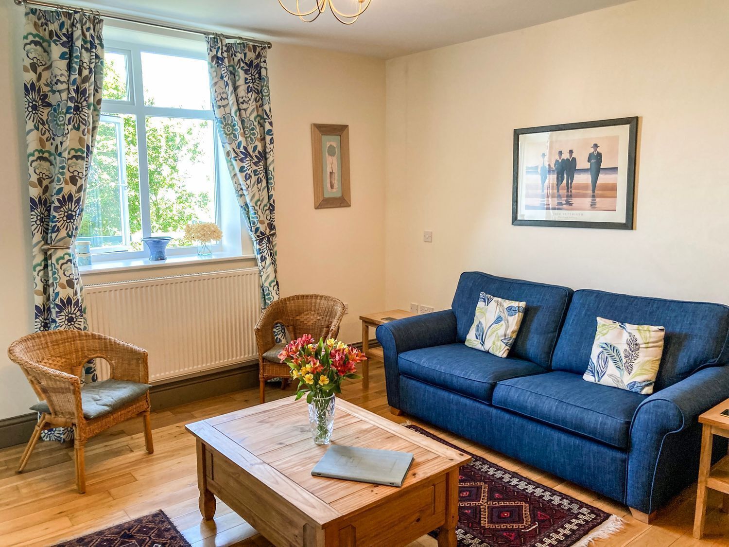 A living room with a blue sofa, wicker chairs, a wooden coffee table, and a vase of flowers.