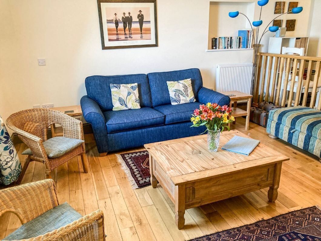 A living room with a blue sofa, wicker chairs, a wooden coffee table, and a bookshelf.