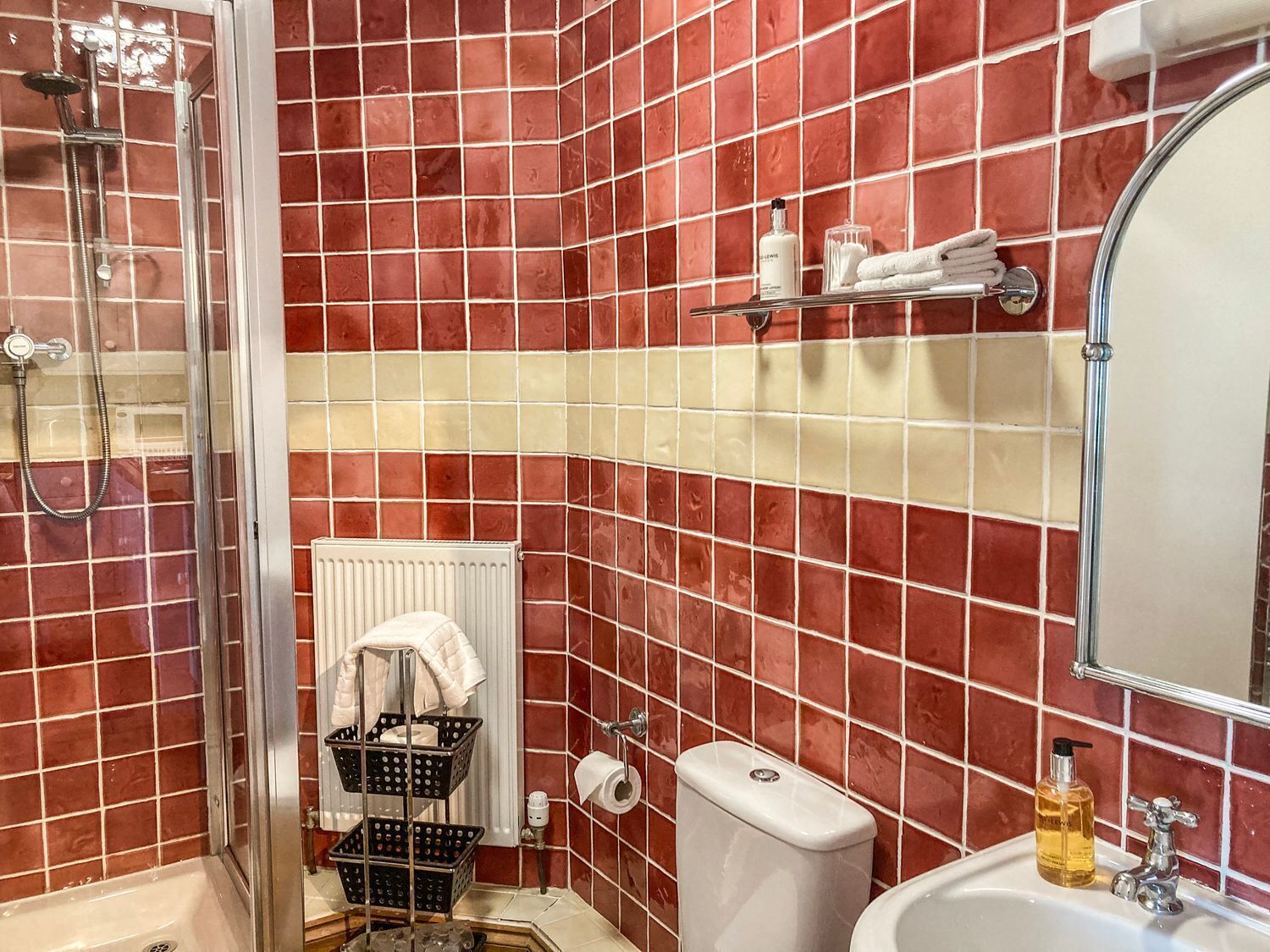 A bathroom with red and beige tiles, a shower, a toilet, a sink, and a mirror.