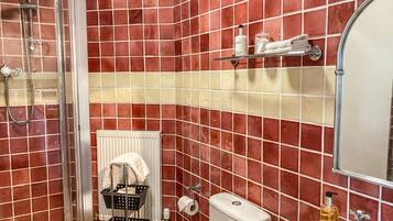 A bathroom with red and beige tiles, a shower, a toilet, a sink, and a mirror.