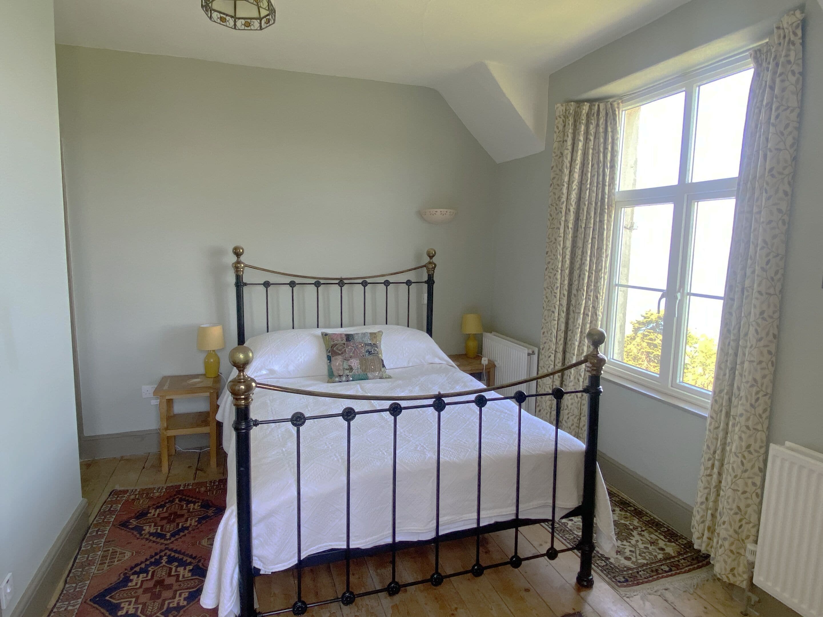 A bedroom with a bed, two bedside tables, a window with curtains, and a radiator.