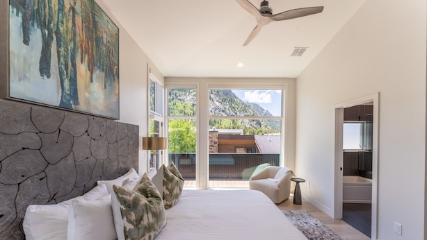 A bedroom with a large bed, a stone headboard, a ceiling fan, and a view of mountains through large windows. - Minutes from Frisco Main Street, 3 Balconies with Panoramic Mountain Views (Frisco)