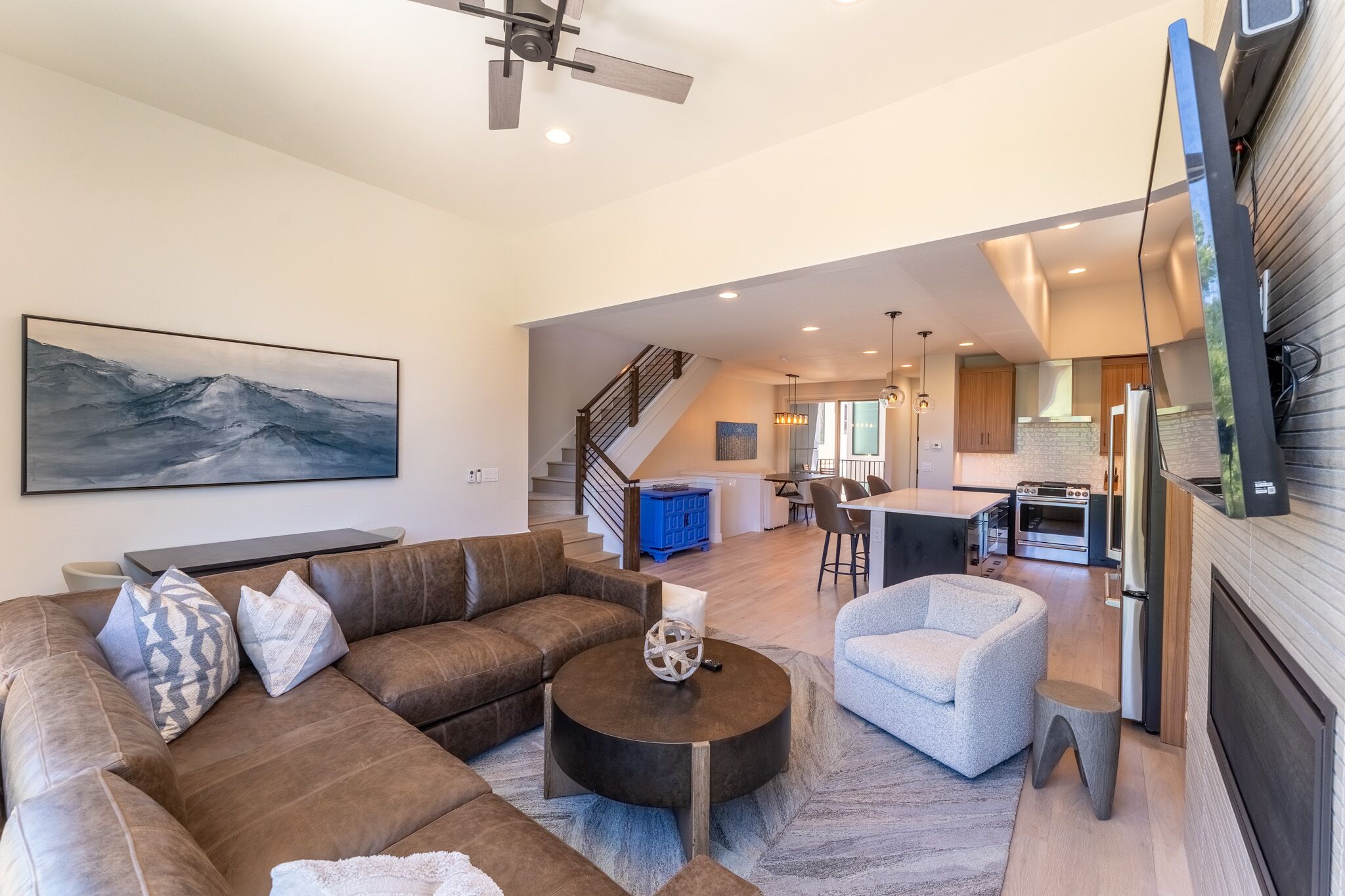 A modern living room with a sectional sofa, a coffee table, and a dining area with a kitchen in the background.