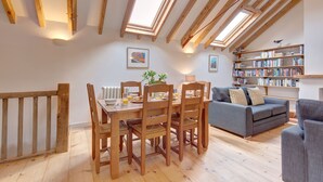 A loft-style room with a dining table, chairs, a sofa, and a bookshelf. - Owl Barn -  a self catering cottage that sleeps 6 guests  in 3 bedrooms (Morston)