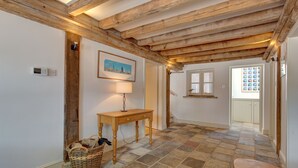 A hallway with exposed wooden beams, a stone-tiled floor, a wooden bench, a wicker basket, and a table with a lamp. - Owl Barn -  a self catering cottage that sleeps 6 guests  in 3 bedrooms (Morston)