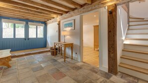 A room with a stone floor, a wooden table, a lamp, and a staircase. - Owl Barn -  a self catering cottage that sleeps 6 guests  in 3 bedrooms (Morston)