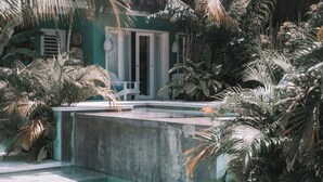 Un espace piscine bordé d’une margelle en béton, entouré d’une végétation tropicale luxuriante et agrémenté d’une chaise blanche.