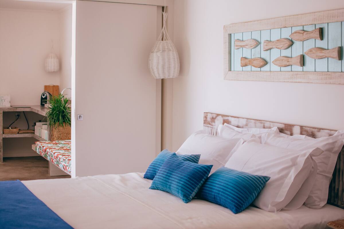 Un dormitorio con una cama, almohadas, una lámpara colgante, una obra de arte en la pared y una pequeña mesa con una planta.