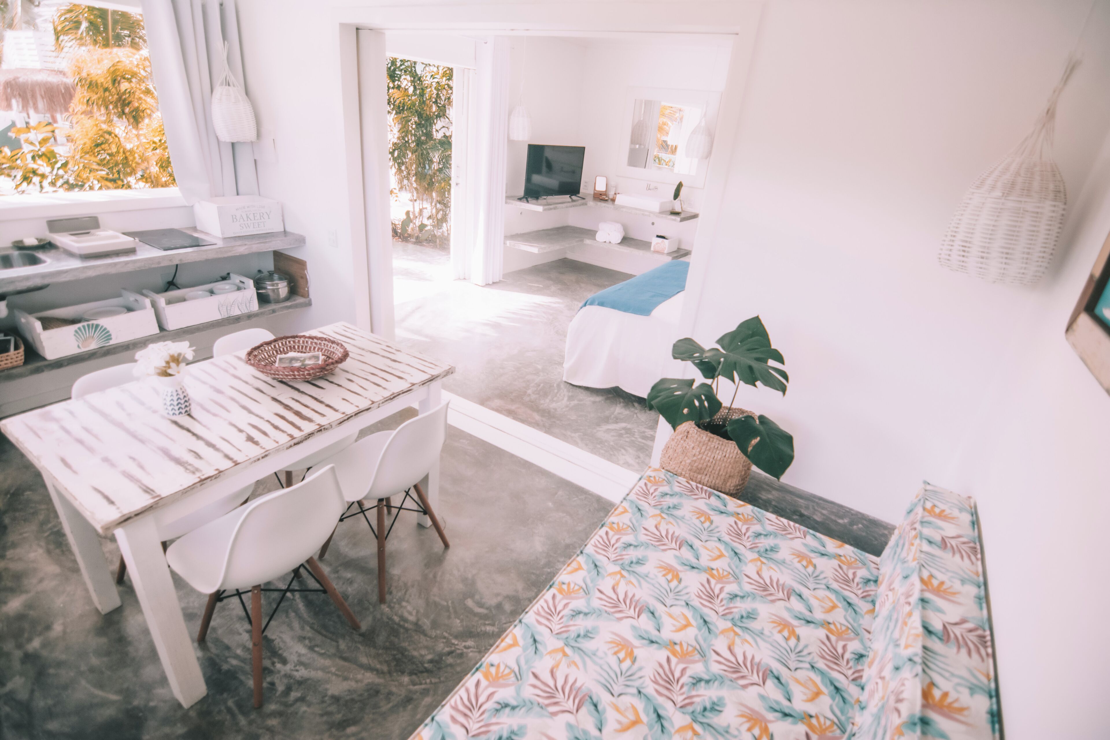 A modern bedroom with a bed, a desk, and a chair. There is a window with a view of trees and a balcony.