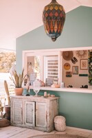 A room with a teal wall, a window with blinds, a potted plant, a decorative lantern, and a shelf with various items including a hat and a framed picture.