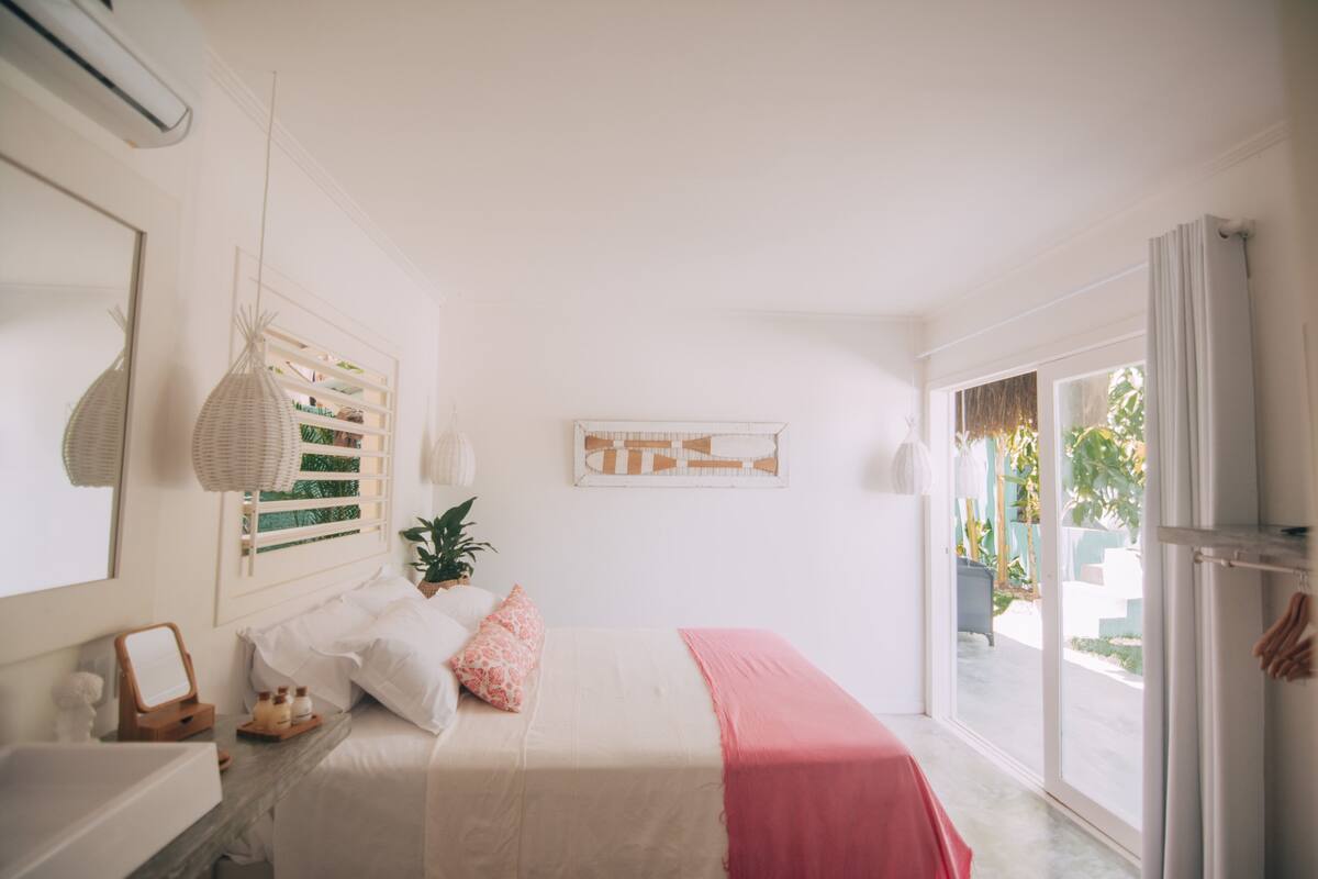 Un dormitorio con cama, mesita de noche, espejo, lámpara colgante y ventana.